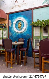 Artwork Of A Golden Sea Horse In A White Circle On The Wall Behind The Tables And Bar Stools Of A Cozy Bar In Willemstad, Curacao