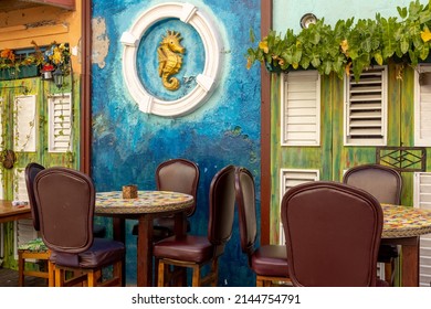 Artwork Of A Golden Sea Horse In A White Circle On The Wall Behind The Tables And Bar Stools Of A Cozy Bar In Willemstad, Curacao