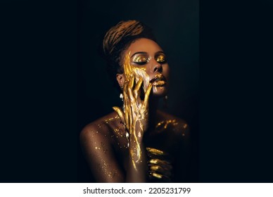 Artwork Portrait Closeup Fantasy African Woman Face In Gold Paint. Golden Shiny Skin. Fashion Model Girl Goddess. Hand Fingers In Metallic Liquid Drop. Arab Royal Style Professional Glamorous Makeup.