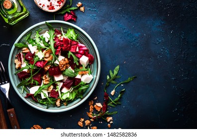 Arugula, Beet and cheese salad with fresh radicchio and walnuts on plate with fork, dressing and spices on blue kitchen table background, place for text, top view