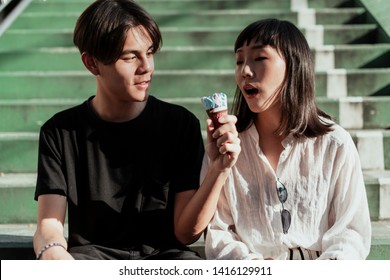 Asain couple eating ice cream cone together against green stairs background