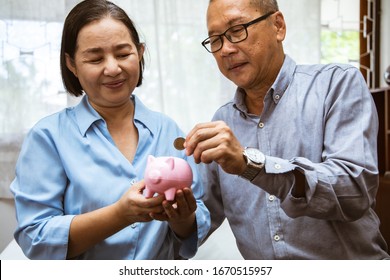 Asain Elder  Putting Coin Money To Piggy Bank Saving, Family, Savings, Age And People Concept - Smiling Senior Couple With Money And Piggy Bank At Home.