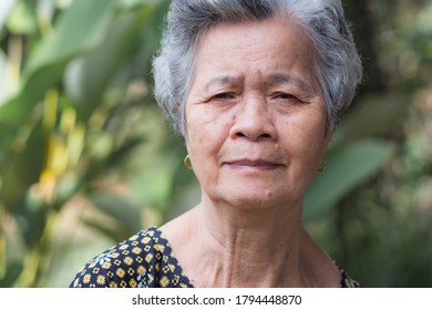 Asain Elderly Woman Smiling And Looking At Camera While Standing In A Garden. Space For Text. Concept Of Old People And Healthcare