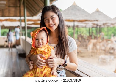 Asain Mom Holding Baby In Her Arm  Looking At Camera Smile And Happiness In Zoo Park. Mother Taking Her Baby Boy To Zoo For Learning And Looking Animal To Development Baby Skill Excited And Cheerful