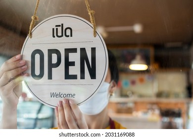 Asain Staff Woman Wearing Protection Face Mask Turning Open Sign Board With Thai Language On Glass Door In Cafe Coffee Shop, Hotel Service, Cafe Restaurant, Retail Store, Small Business Owner Concept