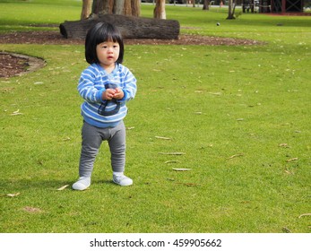 An Asain Toddler Is Standing In The Park, Ready For Her Playtime