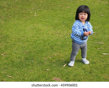 An Asain Toddler Is Standing In The Park, Ready For Her Playtime