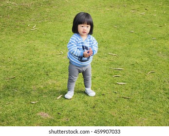 An Asain Toddler Is Standing In The Park, Ready For Her Playtime