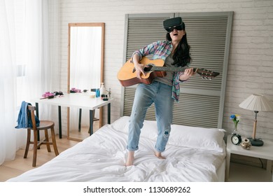 Asain Woman Holding Her Wooden Guitar And Follow The Beat Swaying On Her Bed In Her Bedroom.