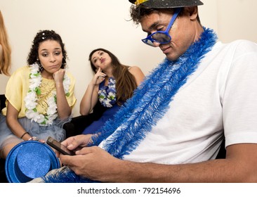 Ash Wednesday After The Carnaval. End Of The Party. Friends Are Tired Of Partying. Brazilian Man Is Using His Cell Phone. In The Background Your Friends Are Sad About The End Of The Holiday.