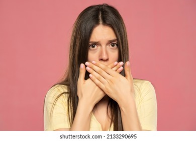 Ashamed woman with hand over mouth on a pink background