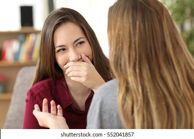 Ashamed Woman Hiding Her Smile In A Conversation With A Friend Sitting On A Couch At Home