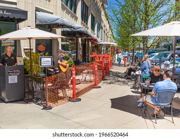 ASHEVILLE, NC, USA-1 MAY 2021: People sitting at sidewalk tables and benches at Carmel's on Page St. on a sunny, spring day.  A couple  Protective masks visible.  Musician.