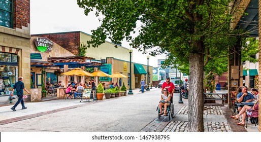ASHEVILLE, NC, USA-27 JULY 2019: Wall Street in downtown is busy on a summer  Sunday, with small crowds at cafe tables, while a man pushes a young woman in a wheel chair.