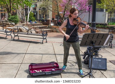 ASHEVILLE, NC, USA-4/11/19: A busker plays a violin (fiddle) in a downtown park on a sunny early spring day.
