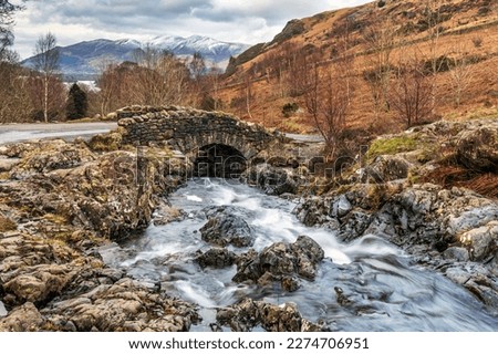 Ashness Bridge, with the snow covered mountain of Skiddaw in the distance, near Keswick and Derwent Water in the Lake District National Park, England.