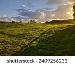 Ashton court estate in Bristol England at sunset in early autumn with setting sun illuminating the grass and clouds with orange light, and shadow formed by tree out of the frame