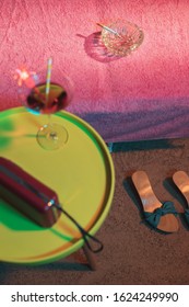 Ashtray With Burning Cigarette On Sunbed With Vintage 1950s Ladies Shoes And Yellow Table With Cocktail And Radio Next To It.