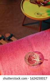 Ashtray With Burning Cigarette On Sunbed With Vintage 1950s Ladies Shoes And Yellow Table With Cocktail And Radio Next To It.