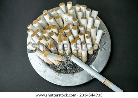 ashtray of a heavy smoker with a lot of cigarette butts, unhealthy lifestyle concept on black background