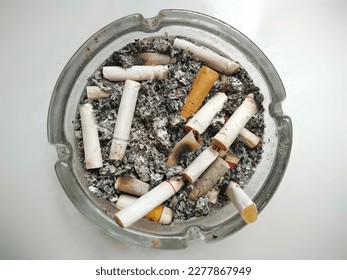 An ashtray made of glass full of cigarette butts and ashes 