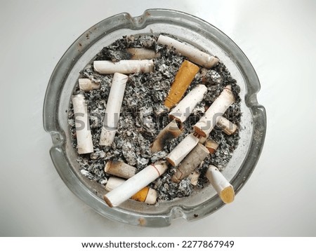 An ashtray made of glass full of cigarette butts and ashes 