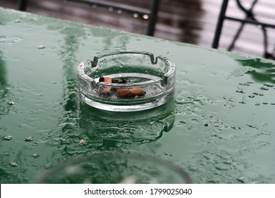 An Ashtray On The Wet Table In A Beer Garden During The Rain, The Rest Of Cigarette Lies In The Inside