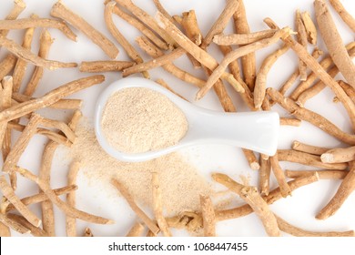 Ashwagandha powder in spoon with ashwagandha roots on white background from above.