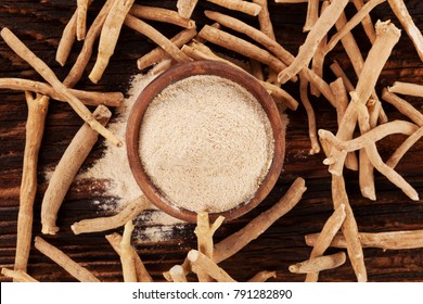 Ashwagandha roots and powder in wooden bowl on wooden table from above. Flat lay. Top shot.