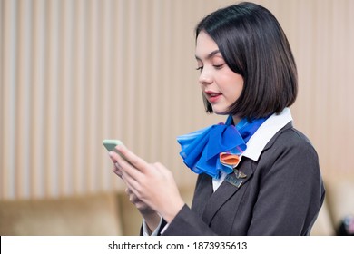 Asia attractive beautiful flight attendant,stewardess playing a smartphone in the airport lobby. Wearing in a brown uniform and sincere smile. Social network, online, and business concept. - Powered by Shutterstock