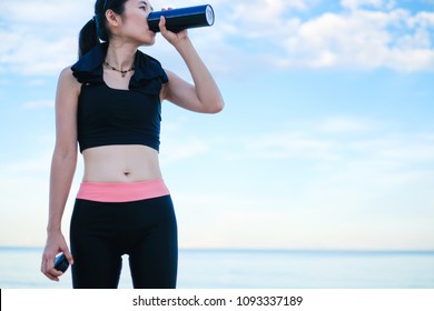 Asia Beautiful Woman In Sport Ware Standing On The Beach And Drinking Whey Protein After Exercise. 