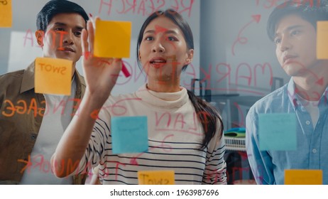 Asia businesspeople stand behind transparent glass wall listen manager pointing progress work and brainstorm meeting and worker post sticky note on wall at office. Business inspiration, Share ideas. - Powered by Shutterstock