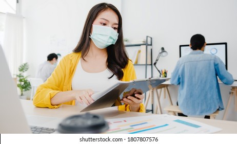 Asia Businesswoman Entrepreneur Wearing Medical Face Mask For Social Distancing In New Normal Situation For Virus Prevention While Using Laptop Back At Work In Office. Lifestyle After Corona Virus.