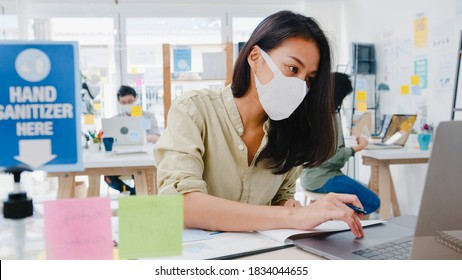 Asia Businesswoman Entrepreneur Wearing Medical Face Mask For Social Distancing In New Normal Situation For Virus Prevention While Using Laptop Back At Work In Office. Life And Work After Coronavirus.