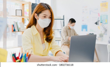 Asia Female Wear Face Mask For Social Distancing In New Normal Situation For Virus Prevention While Using Laptop And Separated By Acrylic Partition Stand In Office. Life And Work After Corona Virus.