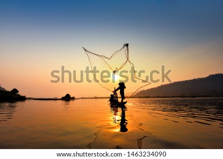 Asia fisherman net using on wooden boat casting net sunset or sunrise in the Mekong river - Silhouette fisherman boat with mountain background life person countryside 