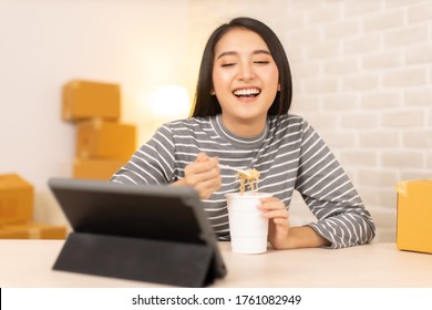 Asia Freelance  Business Woman Eating Instant Noodles While Working On Laptop In Living Room At Home Office At Night. Young Asian Girl Sitting On Desk Work Overtime, Enjoy Relax Time.female Working .