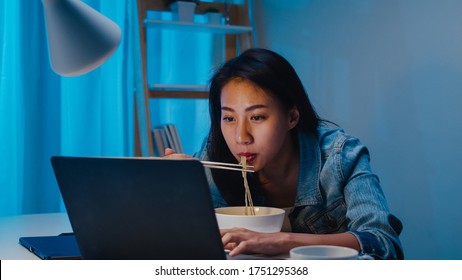 Asia freelance smart business women eating instant noodles while working on laptop in living room at home at night. Happy young Asian girl sitting on desk work overtime, enjoy relax time. - Shutterstock ID 1751295368