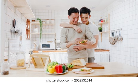 Asia gay couple using tablet and preparing the breakfast, sandwich vegetable on table in kitchen at home. Young LGBT men talking happy relax rest together spend romantic time at house in morning. - Powered by Shutterstock