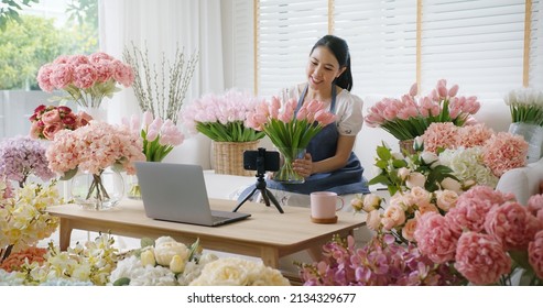 Asia girl vlogger influencer or SME owner people smile work on home video camera selfie shoot filming for live sell show happy talk on mobile VoIP app. Remote sale product at modern florist gift shop.