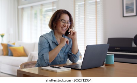 Asia Healthy Elder People, SME Owner Lady Or Latin Telesale Service Agent Manager Answer Cellphone Call Via 5G Wifi Wireless Relax Sit At Home Office Desk With Smile Humor Laugh Client Care Job.