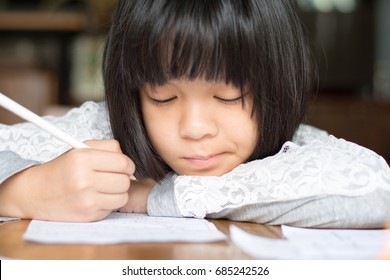 Asia Kid Girl Doing Homework With Thinking Face At Home. Female Cute Child Concentrate Write On Paper. Asian Students Practice Math Subject For Test. Student Study At House