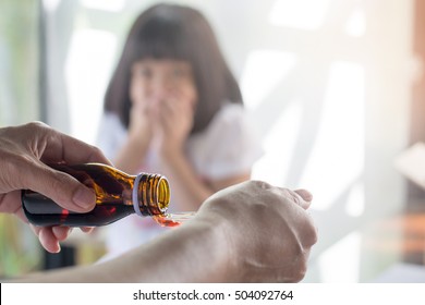 Asia Little Child Girl Hand Close On Her Mouth Do Not Want To Take Medicine For Mother. Asian Kid Female Refuse To Eat Drug. Hands Of Mom Pouring Cough Syrup Medicine Into Clear Spoon To Daughter.