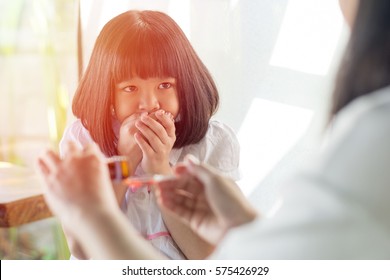 Asia Little Child Girl Hand Close On Her Mouth Do Not Want To Take Medicine For Mother. Asian Kid Female Refuse To Eat Drug. Hands Of Mom Pouring Cough Syrup Medicine Into Clear Spoon To Daughter.