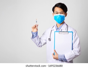 Asia Man Doctor Wearing Surgical Mask And Hand Holding Vaccine Syringe And Paper Form Standing In Gray Wall Background. Concept Preventive Measures Against Corona Virus.