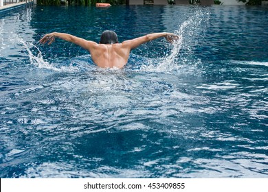 Asia Man Doing Butterfly Strokes While Swimming With Splash Of Water Pool. View Of Back Male Swimmer Performing The Butterfly Stroke At Outdoor Swimming Pool. Asian Thailand. 