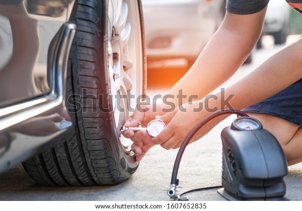 Asia man use Tire gauge\
analog check air pressure of wheel car on the road basic\
maintenance by oneself