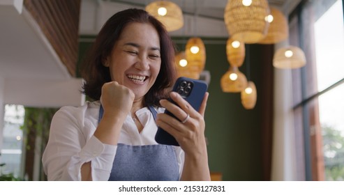 Asia mature adult woman people wear apron small cafe receive e-mail text good news SME lending service solution win seller store in social media app. Shock smile laugh face in sale order reopen shop. - Shutterstock ID 2153127831