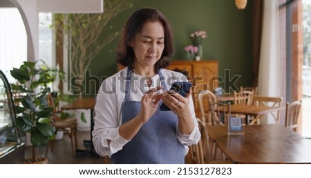 Asia mature adult woman people wear apron small cafe receive e-mail text good news SME lending service solution win seller store in social media app. Shock smile laugh face in sale order reopen shop.