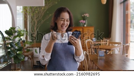 Asia mature adult woman people wear apron small cafe receive e-mail text good news SME lending service solution win seller store in social media app. Shock smile laugh face in sale order reopen shop.